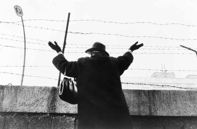 An elderly woman, standing at Berlin Wall, in west sector, with hands raised, after waiting three hours to see her East Berlin friends and relatives (1961).